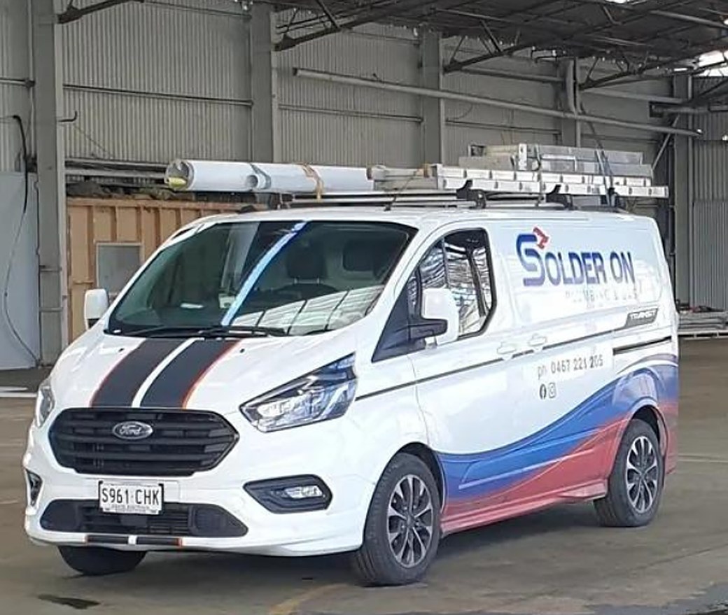 The Solder On Plumbing & Gas van, a white Ford Transit wrapped in the navy and red logo, with pipe racks on the roof